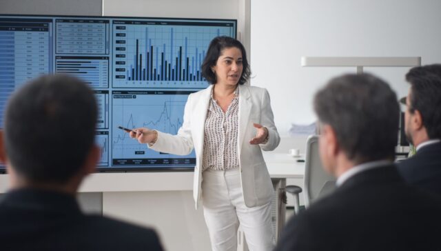Businesswoman presenting financial charts to a group of colleagues in a conference room, representing stock analysis