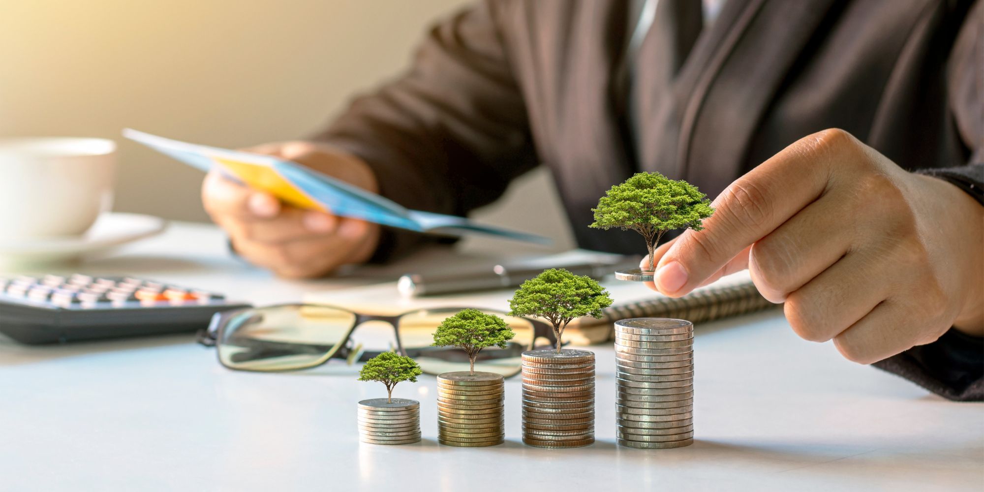 Hands stacking coins with small plants growing on them, symbolizing long-term investment growth