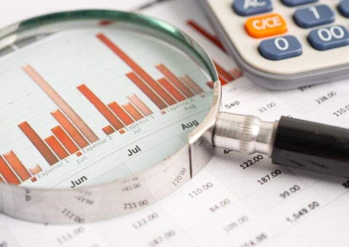 Magnifying glass highlighting a bar chart with a calculator, representing stock market analysis