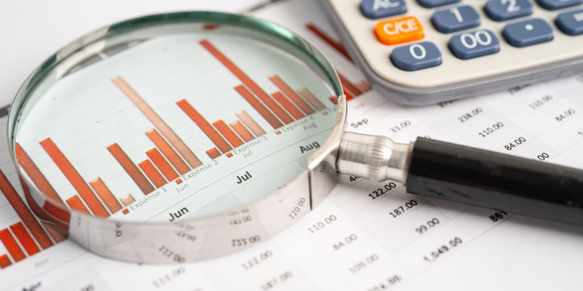 Magnifying glass highlighting a bar chart with a calculator, representing stock market analysis
